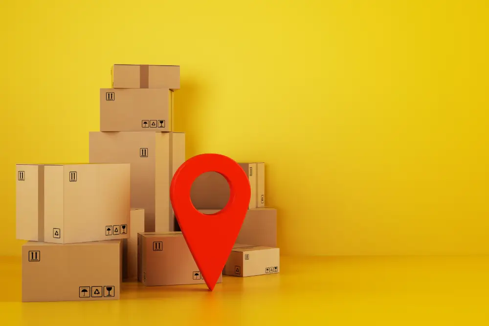 A large red location pin standing among stacked cardboard boxes on a yellow background