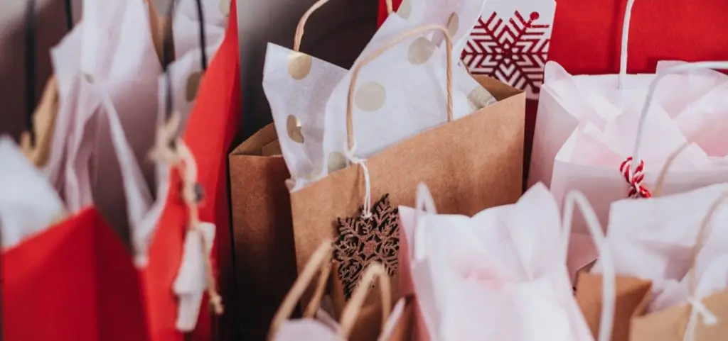 A cluster of red, white and kraft paper gift bags stuffed with tissue, some tagged with snowflakes for the holidays