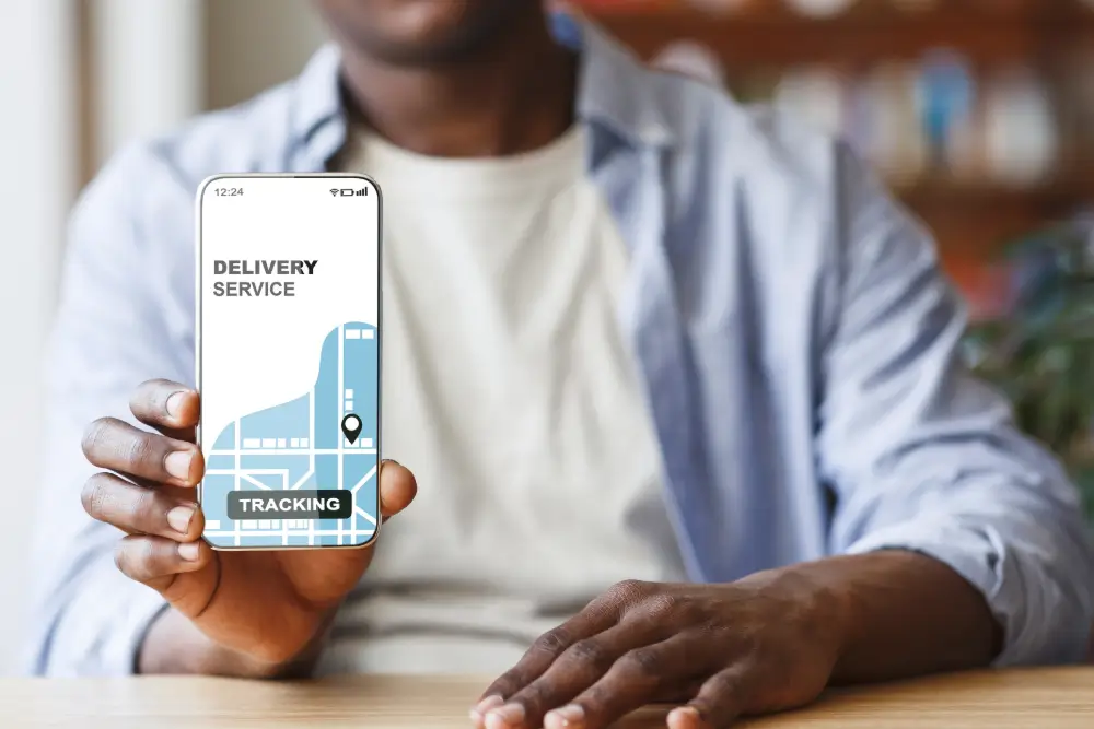 Someone holding out a phone showing a delivery service tracking screen with a map and a location pin