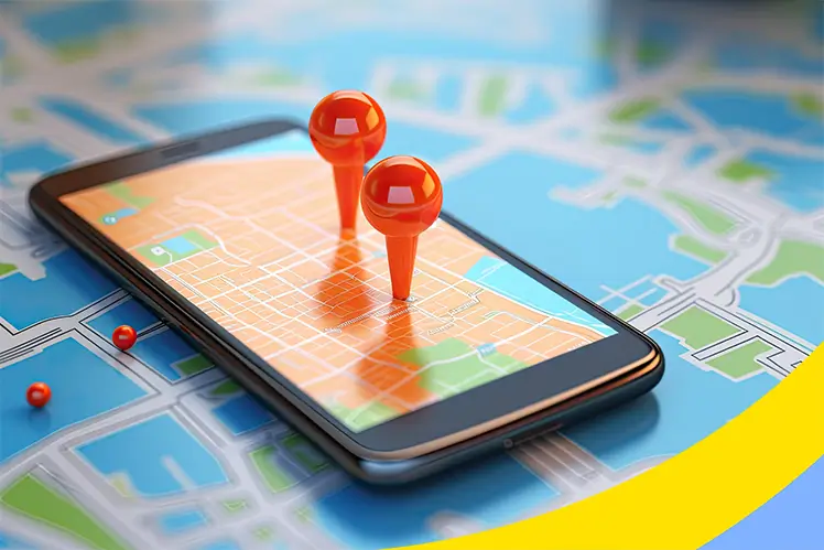 Two orange map pins standing on a phone showing a street map, laid on a larger printed map