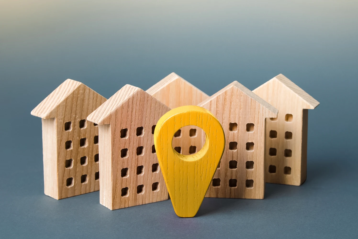 A yellow wooden location pin standing among five model wooden houses